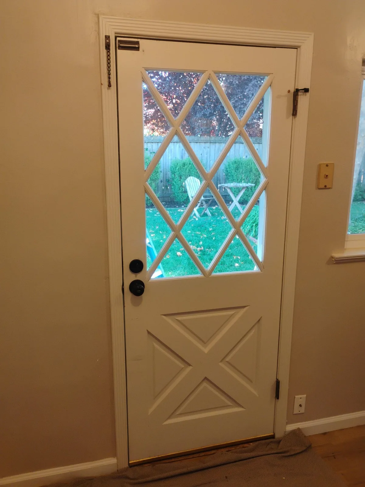 Inside view of the dated white entry door with diamond-grid glass and a crossbuck lower panel before replacement in Pleasant Hill, CA