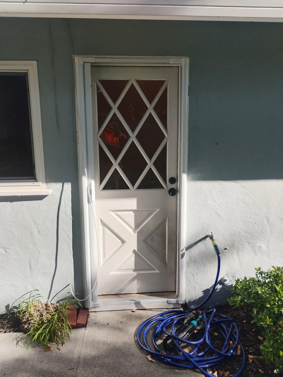 Original white rear kitchen entry door with a storm door and diamond-grid glass before replacement in Pleasant Hill, CA